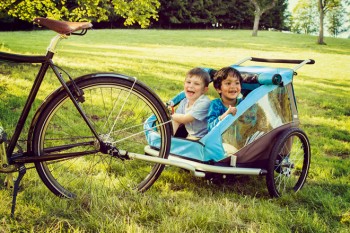 Zwei Kinder sitzen im Fahrradanhänegr für Kinder.