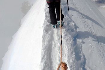 Bergsteiger-F&uuml;&szlig;e in einer schmalen Schneespur auf einem Gratweg.