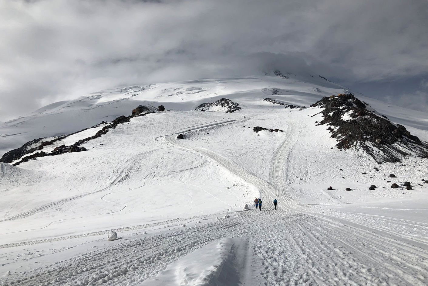 Bekannter Anblick bei der Besteigung des Elbrus: Die Schneemobil-Spuren ziehen Richtung Pastuchkov-Felsen - und an der abgebrannten Priut 11-Hüte (links im Bild) vorbei. | Foto: Michael Hrobath