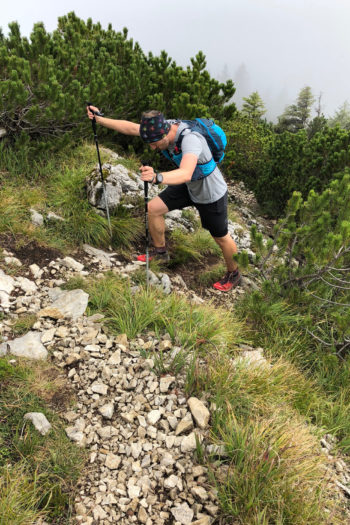 Trailrunner läuft mit Trailrunningstöcken den Berg hoch.