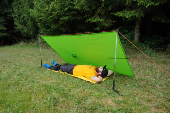Mann liegt nach dem Tarp aufbauen unter dem stabilem Regenschutz.