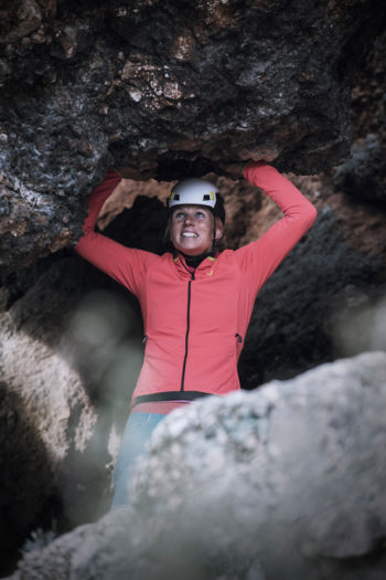 Eine Frua mit Kletterhelm st&uuml;tzt sich mit den H&auml;nden von unten gegen einen Felsvorsprung.