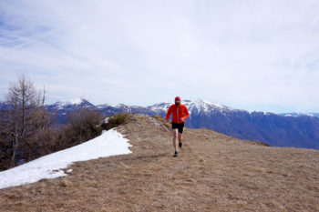 Trailrunner l&auml;uft auf Bergwiese auf die Kamera zu