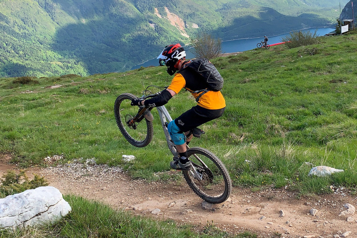 Mountainbiker macht Wheelie auf einem Trail mit Blick auf Molvenosee
