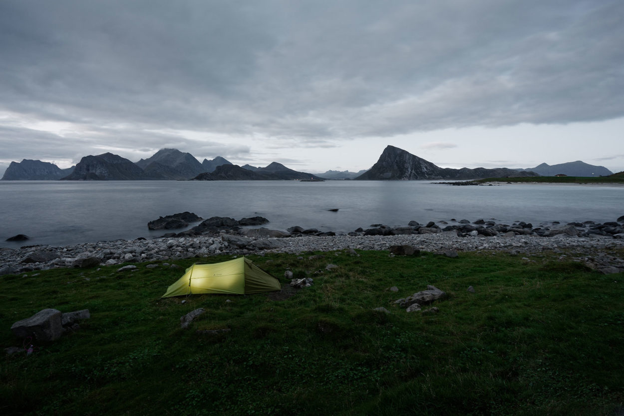 Grünes, beleuchtetes Zelt in Dämmerung auf Wiese an norwegischer Küste