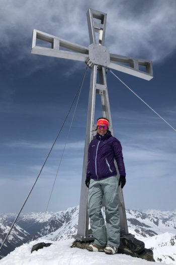 Eine Frau in Skitourenbekleidung am Gipfelkreuz im Schnee.