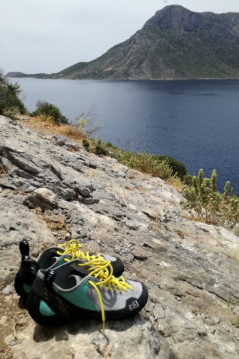 Kletterschuhe stehen auf Fels mit Blick auf Meeresbucht und vorgelagerte bergige Insel
