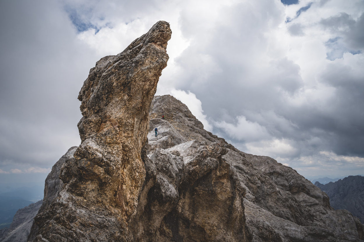 Spitze Felsnase ragt aus Felsmassiv, Bergsteiger im Hintergrund