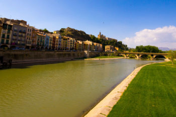 Fluss in Stadt mit Wiese an Ufer und am anderen Ufer spanischen Häusern