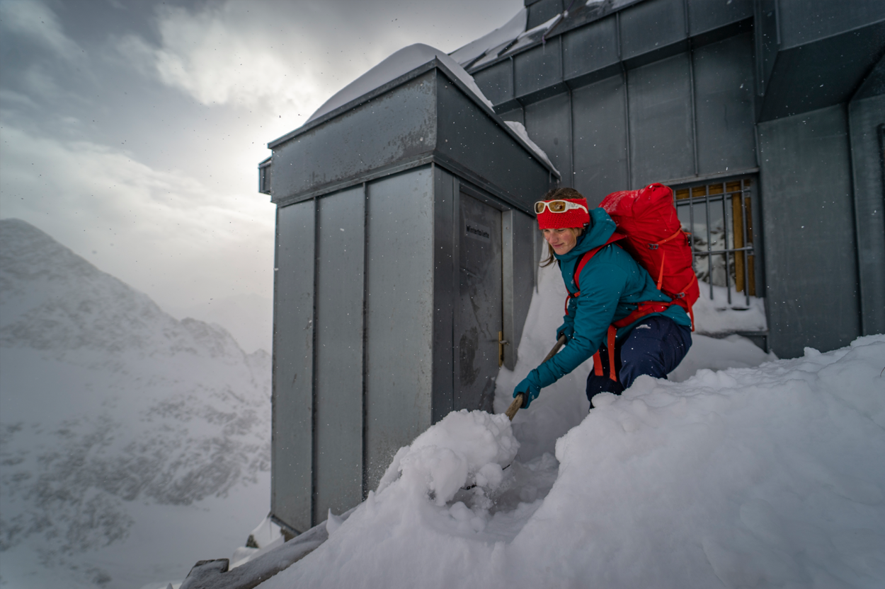 Frau schaufelt Tür von Berghütte frei von Schnee