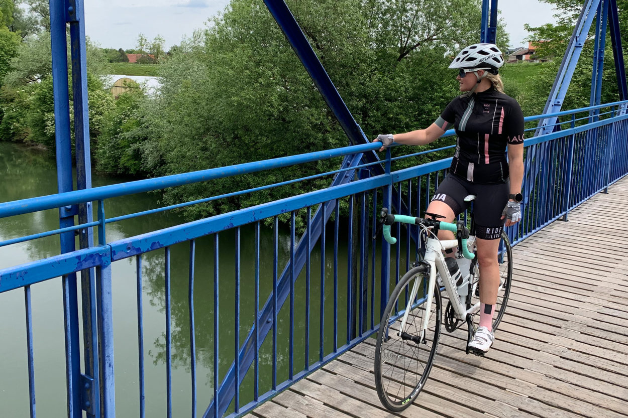 Rennradfahrerin hält sich am Geländer einen blauen Brücke fest.