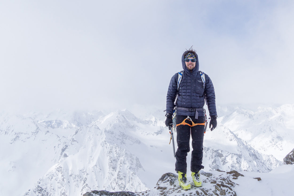 Franz Güntner auf dem Gipfel, im Hintergrund schneebedeckte Berge.